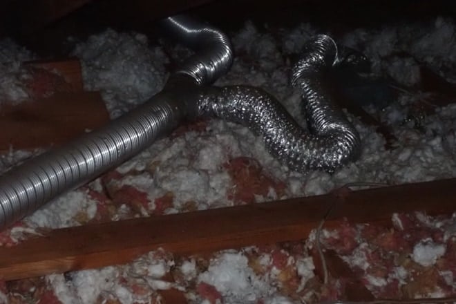 Attic with silver flexible ducting resting on insulation, including a contorted duct run that does not exit the attic