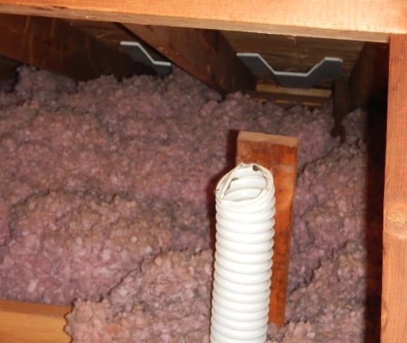 Attic space with pink blown-in insulation and a white flexible exhaust duct ending openly in the attic instead of through an exterior termination