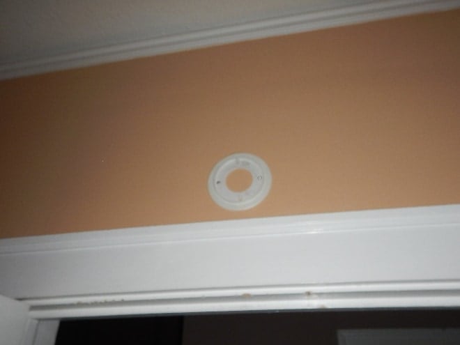 Empty circular smoke-alarm mounting plate on a wall above a doorway with the detector itself removed