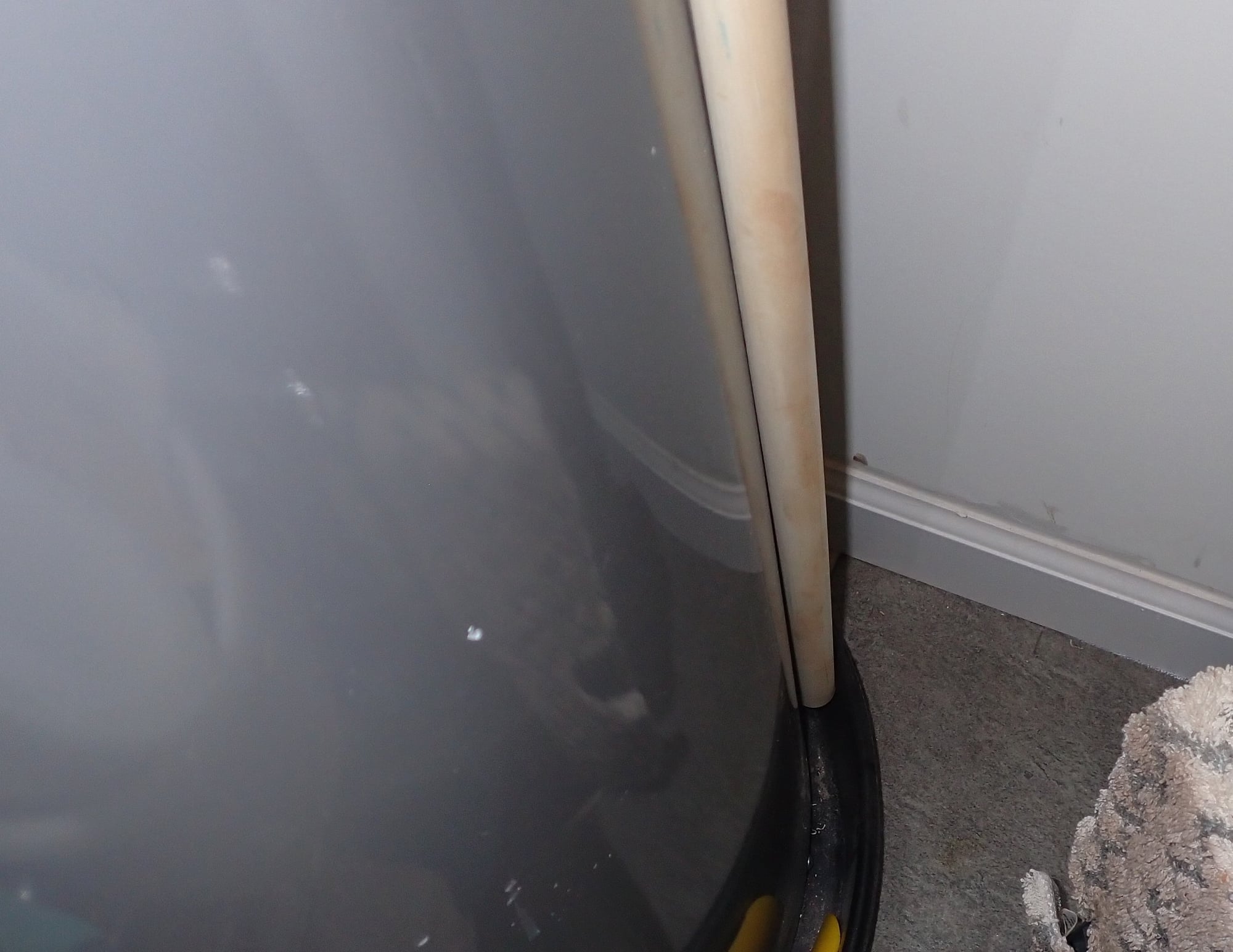 Base of a water heater sitting in a black drain pan with a light-colored discharge pipe ending inside the pan