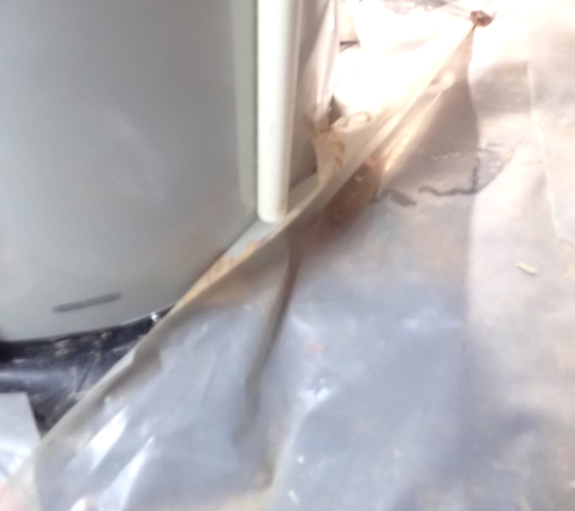 Lower portion of a water heater in a crawlspace with a white discharge pipe ending just above the vapor barrier