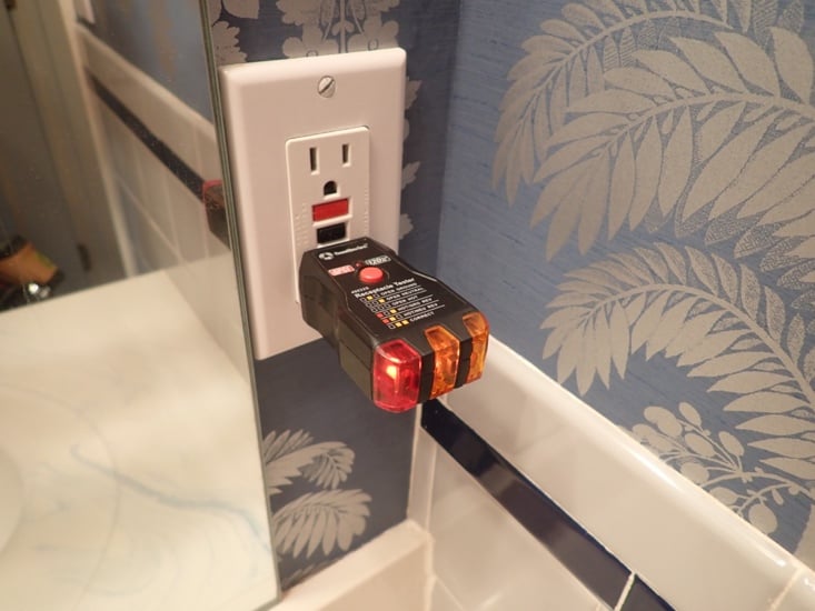 A plug-in receptacle tester in a three-prong outlet showing an open-ground fault indication