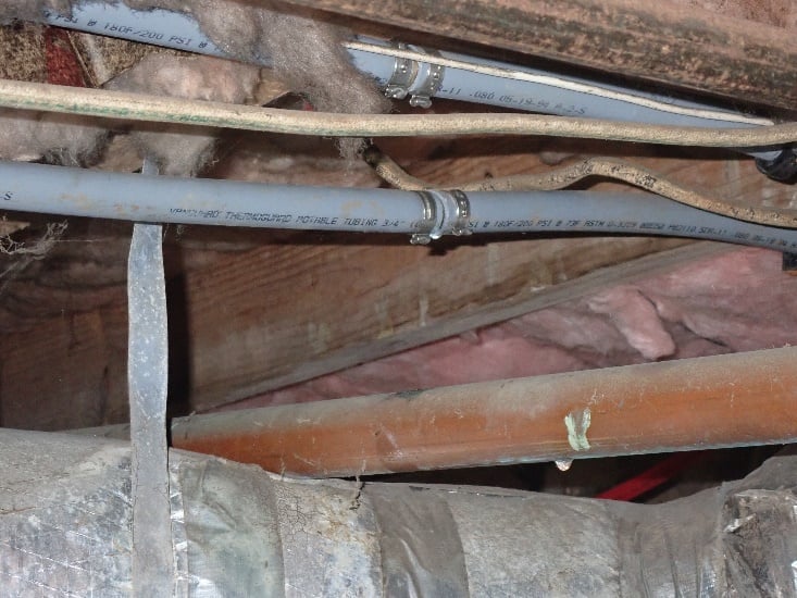 Gray polybutylene potable water tubing routed through a crawlspace with a fitting