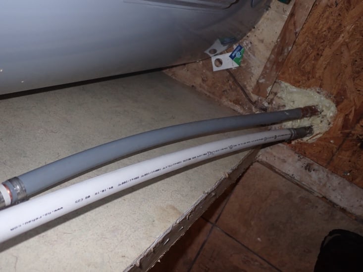 Gray polybutylene supply pipe next to a newer white plastic supply pipe near a water heater
