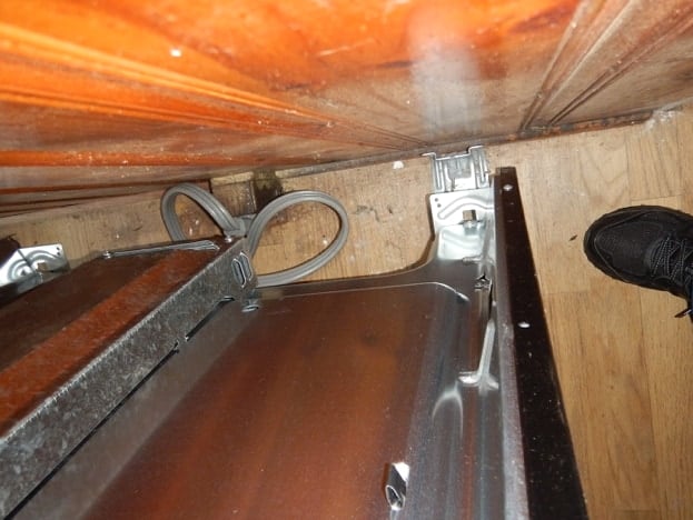 Floor behind a freestanding range showing a metal anti-tip bracket that the range rear foot is not hooked into